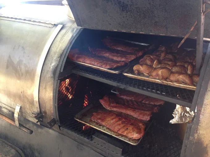 The offset smoker at David's BBQ loaded with racks of ribs and chickens over a live fire.